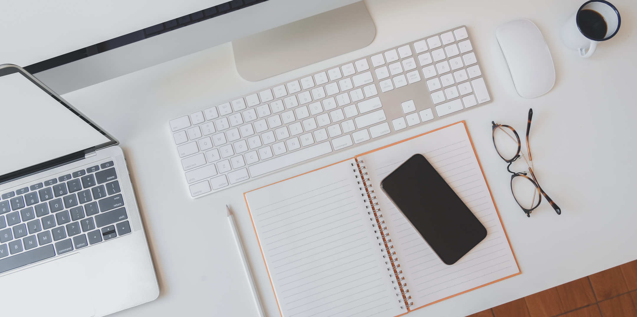 Laptop and computer placed on white work desk with notepad and smartphone